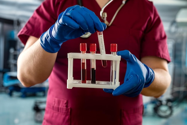 Männlicher Arzt oder Biochemiker trägt rote Uniformhandschuhe von Viruserkrankungen und untersucht Blut in einem Reagenzglas in einem modernen Krankenhaus