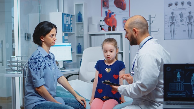 Männlicher Arzt schreibt Kinderdiagnose auf Tablet im Gespräch mit Frau. Heilpraktiker Arzt Facharzt für Medizin, der Gesundheitsdienstleistungen erbringt Beratungsbehandlung im Krankenhaus