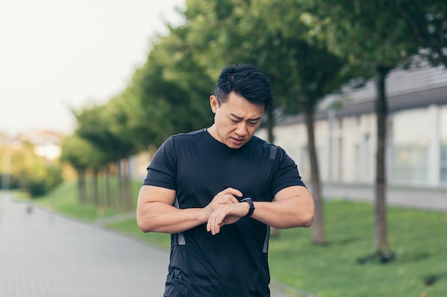 Männlicher asiatischer Athlet, müde nach einem morgendlichen Joggen, läuft im Park in der Nähe des Stadions