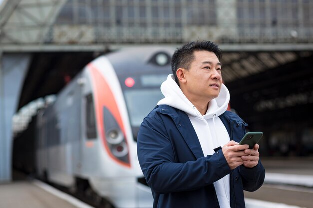 Männlicher asiatischer Geschäftsmann am Bahnhof kauft Zugtickets online mit einem Mobiltelefon und einer Anwendung, die der Tourist von einer Geschäftsreise nach Hause zurückbringt