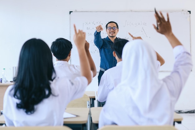 Männlicher asiatischer Highschool-Lehrer steht vor der Klasse und stellt während der Schülererziehung Fragen