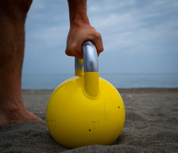 Männlicher Athlet, der am Strand mit Kesselglocken trainiert