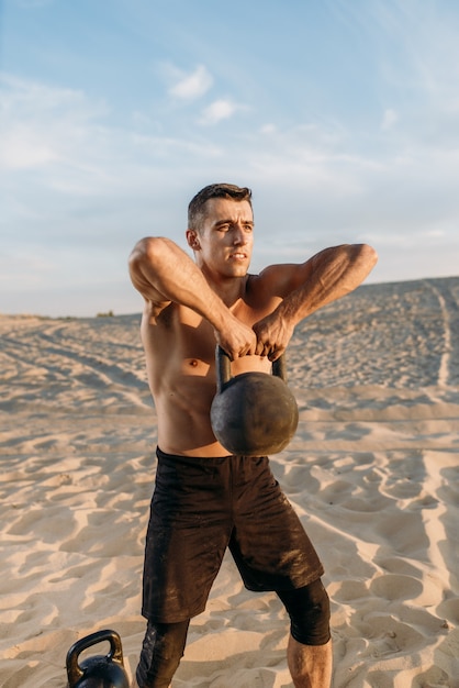 Männlicher Athlet, der auf Sand nach dem Training in der Wüste am sonnigen Tag sitzt. Starke Motivation im Sport, Krafttraining im Freien