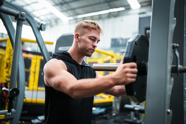 Männlicher Athlet, der im Fitnessstudio trainiert und Gewichte hebt, die Gelenke ziehen