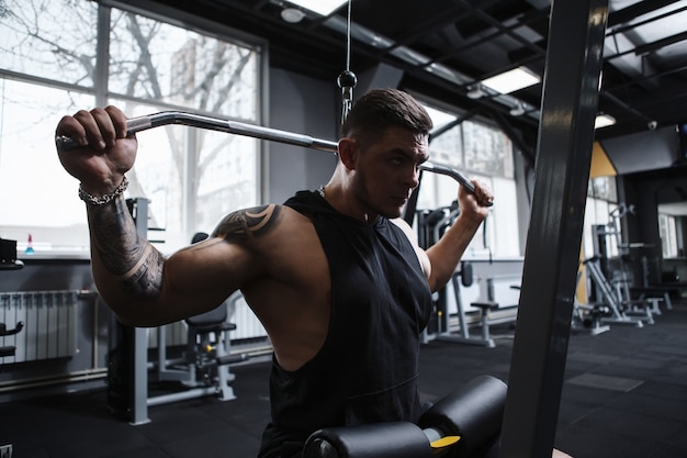 Männlicher Athlet mit muskulösem Körper, der auf vertikalem Rudergerät des lat Pulldowns arbeitet