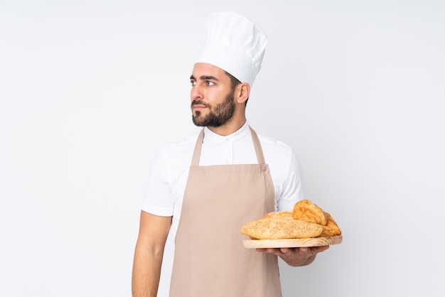 Männlicher Bäcker, der einen Tisch mit mehreren Broten auf weißer Wand schaut Seite hält