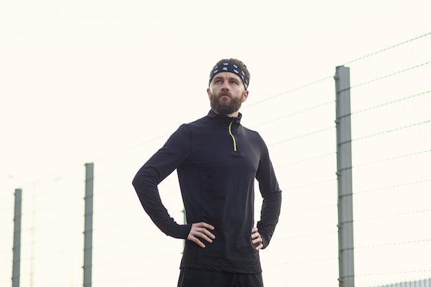 Männlicher bärtiger Athlet in Sportuniform und Bandana nach hartem Training auf dem Spielplatz