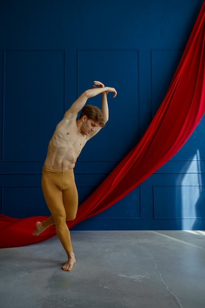 Männlicher Balletttänzer, Ausbildung im Tanzunterricht, blaue Wände und rotes Tuch. Performer mit muskulösem Körper, Anmut und Eleganz der Bewegungen