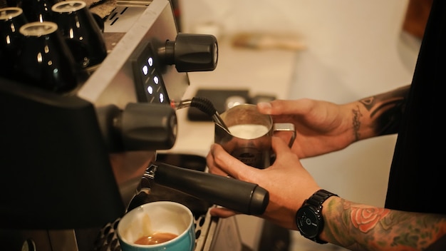 männlicher Barista mit Tätowierungen, die Cappuccinos zubereiten, die Kaffeegetränke zubereiten