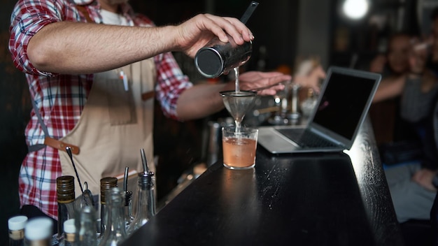 Foto männlicher barkeeper schenkt einen cocktail aus einem shaker ein, bester service