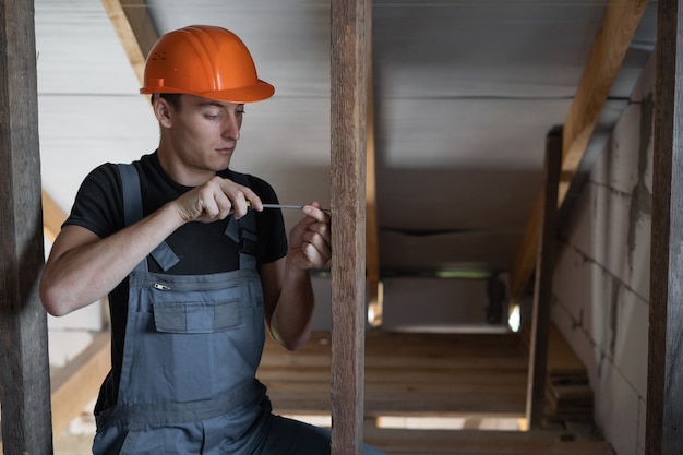 Foto männlicher baumeister in arbeitskleidung und einem orangefarbenen schutzhelm gekleidet. zieht eine selbstschneidende schraube mit einem schraubendreher an. platz kopieren