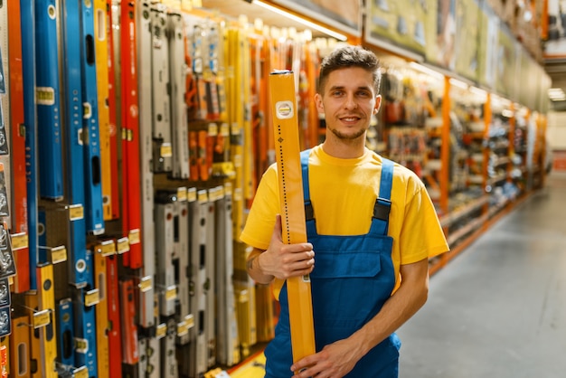 Männlicher Baumeister mit Gebäudeebene im Baumarkt. Konstrukteur in Uniform betrachten die Waren in DIY Shop