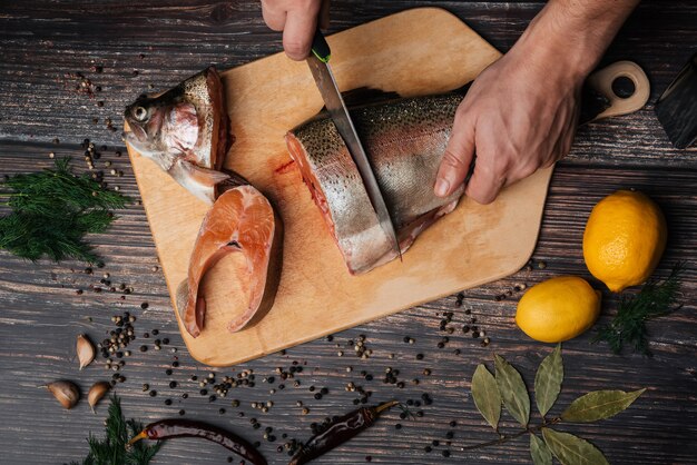 Männlicher Chef schneidet frische rote Fische auf einem Brett auf einem Holztisch