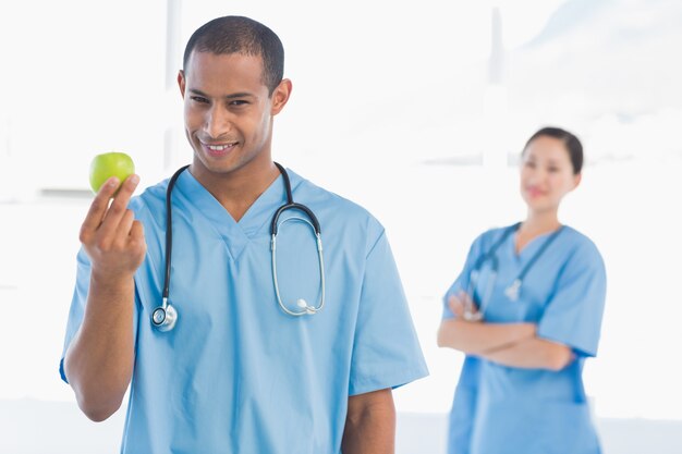 Männlicher Chirurg, der einen Apfel mit Kollegen nach anhält