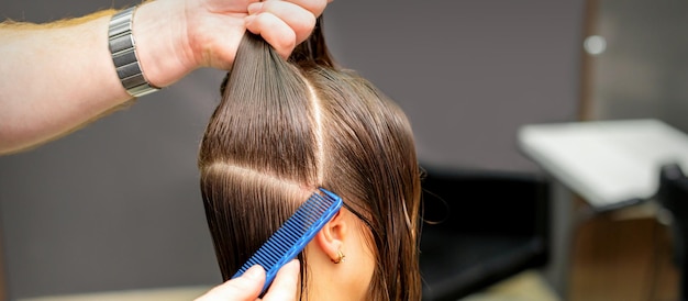 Männlicher Coiffeur teilt Frauenhaare in Abschnitte mit Kamm und Händen in einem Schönheitssalon.