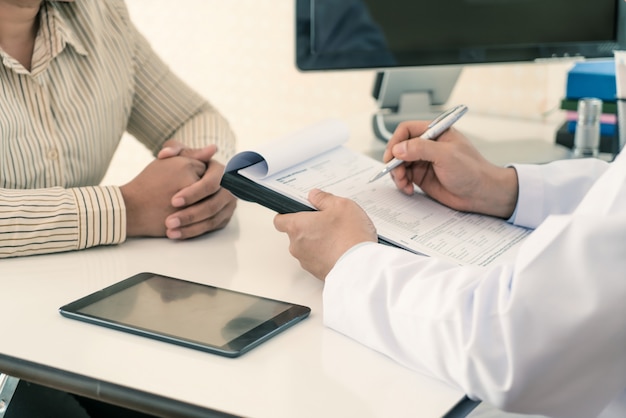 Männlicher Doktor, der Diagnose Patienten erklärt. Frauenpatient, der wenn hörende Bettnachrichten gesorgt schaut.