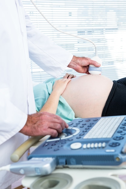 Männlicher Doktor, der Ultraschall auf schwangerer Frau tut