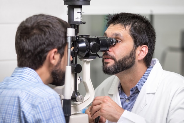 männlicher Doktoraugenarzt überprüft die Augenvision des hübschen jungen Mannes in der modernen Klinik