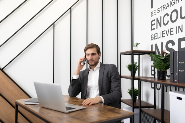 Männlicher Finanzier, der mit Laptop am Tisch sitzt und heiße Anrufe tätigt