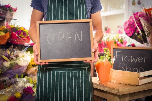 Männlicher Florist, der offenes Zeichen auf Schiefer an seinem Blumenladen hält