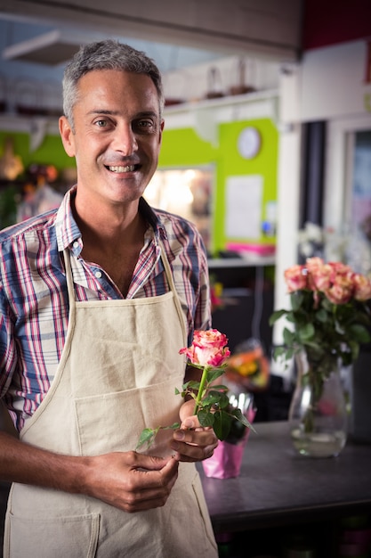 Männlicher Florist, der Rose am Blumenladen hält