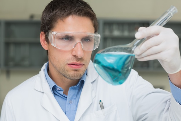 Männlicher Forscher, der Flasche mit blauer Flüssigkeit im Labor betrachtet