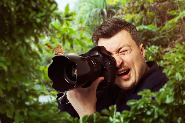 Männlicher fotograf bei der arbeit, schöner schmetterling, der auf der kameralinse, grüner wald sitzt