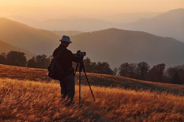 Männlicher Fotograf, der in einer majestätischen Landschaft aus Herbstbäumen und Bergen am Horizont steht und arbeitet