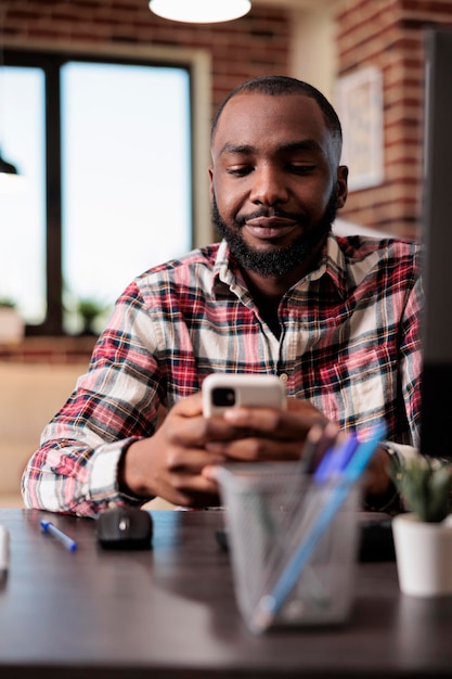 Männlicher Freiberufler, der auf dem Smartphone im Internet surft und bei der Arbeit Website-App und Social-Media-Netzwerk verwendet. Remote-Arbeiten mit dem Mobiltelefon, Online-SMS-Nachrichten im Klassen-Webinar.