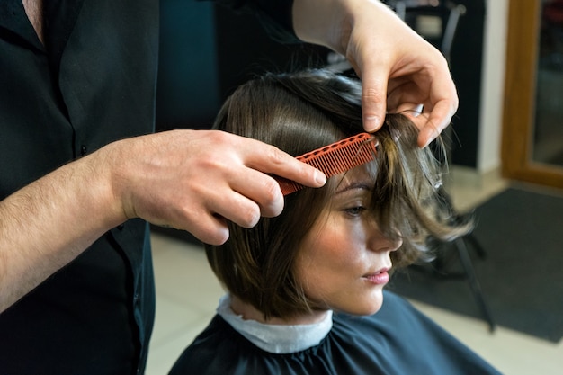 Männlicher Friseur bereitet sich auf den Haarschnitt der schönen Frau im Schönheitssalon vor.