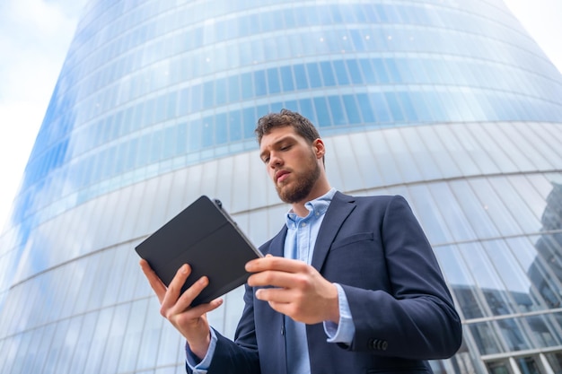 Männlicher Geschäftsmann oder Unternehmer außerhalb des Büros mit einem Tablet in einem Glasgebäude