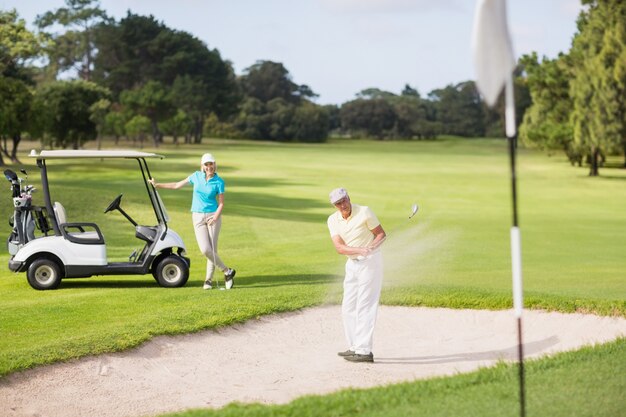 Männlicher Golfer, der auf Sandfalle durch Frau spielt