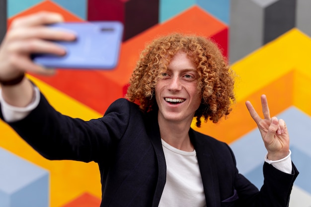 Männlicher Hipster, der selfie gegen bunte Wand nimmt