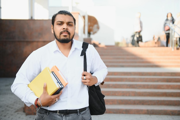 Männlicher indischer Student, der mit Buch an der Universität steht