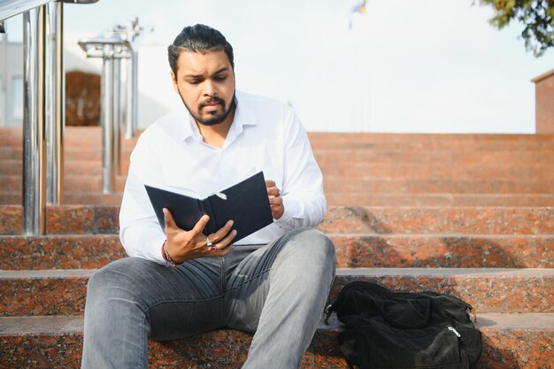 Männlicher indischer Student, der mit Buch an der Universität steht