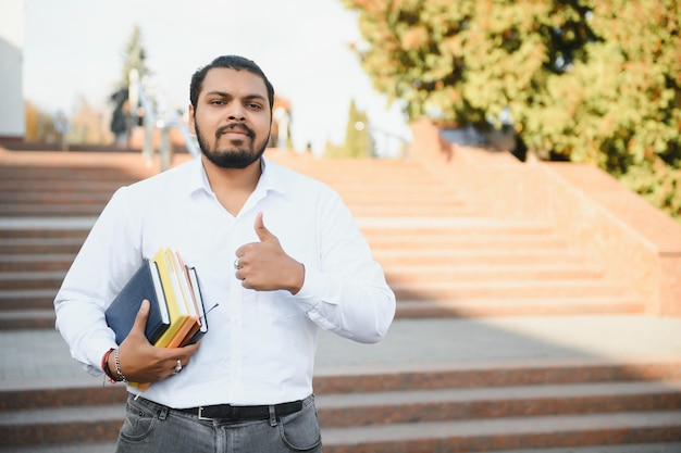 Männlicher indischer Student, der mit Buch an der Universität steht