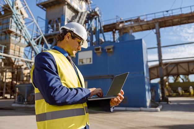 Männlicher Ingenieur, der draußen in der Fabrik an Notebook arbeitet