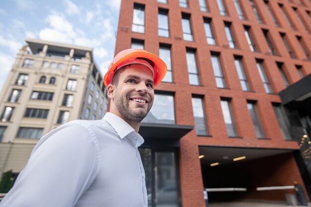 Männlicher Ingenieur im orangefarbenen Helm, der lächelt und zuversichtlich schaut