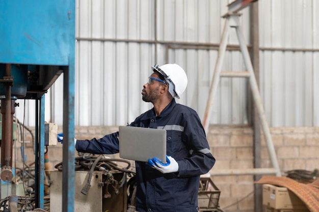 Männlicher Ingenieur in Uniform mit Laptop-Inspektionsmaschine in der Fabrikindustrie