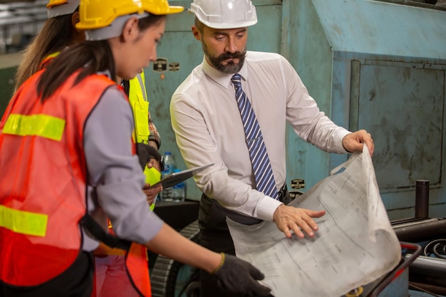 Männlicher Ingenieur und Industriearbeiter in Schutzhelmen diskutieren neues Projekt, während sie einen Laptop verwenden. Sie machen Zeigegesten. Sie arbeiten in einer Fabrik für die Schwerindustrie.