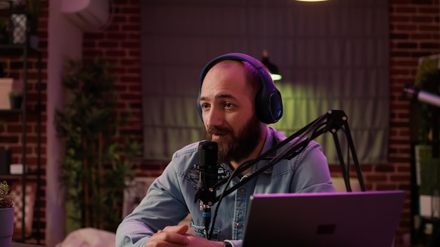 Männlicher Inhaltsersteller, der Vlog mit einer digitalen Videokamera aufzeichnet, während er ein professionelles Mikrofon und einen Audiomischer im Heim-Podcasting-Studio verwendet. Influencer senden Live-Internetradio.