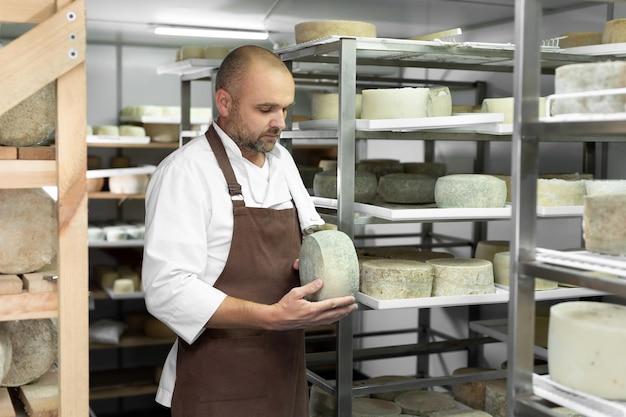 Männlicher Käser kontrolliert die Reifung von Käse in den Regalen im Reifungs- und Lagerraum