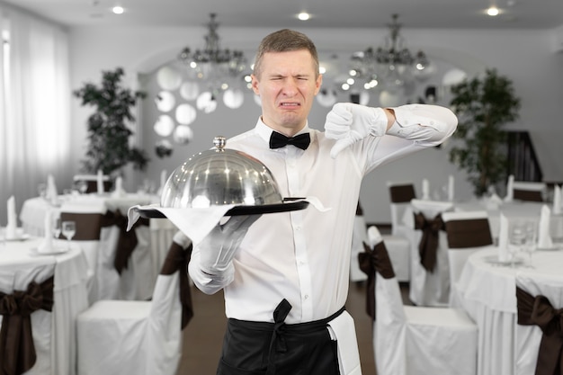 Männlicher Kellner in einem Rstoran mit einem Gericht in der Hand zeigt, dass dieses Gericht geschmacklos ist.