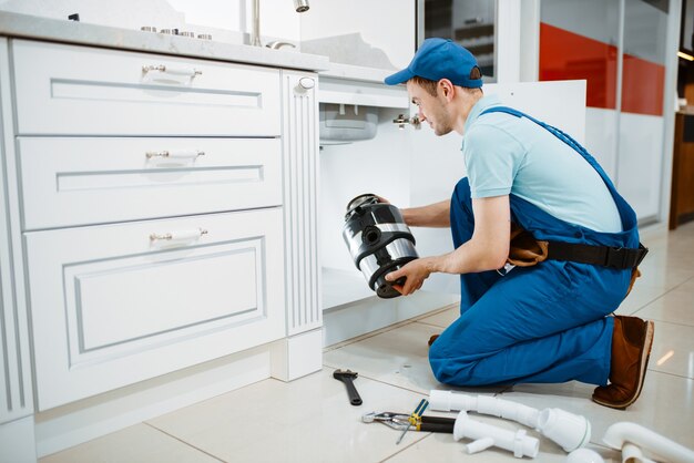 Männlicher Klempner in Uniform, der Entsorger in der Küche installiert. Heimwerkerin mit Werkzeugtaschen-Reparaturspüle, Sanitäranlagen-Service zu Hause