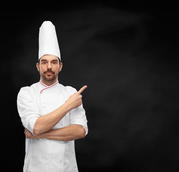 männlicher Koch in Toque, der mit dem Finger auf Schwarz zeigt