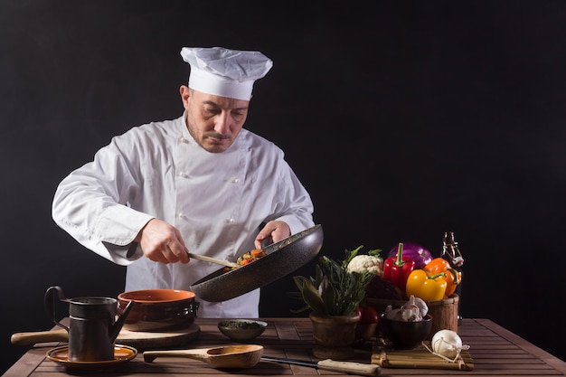 Männlicher Koch in weißer Uniform bereitet Essensteller mit Gemüse zu