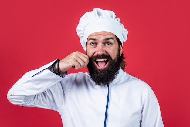 Männlicher Koch mit Hut mit Bart und Schnurrbart auf rotem Hintergrund erfahrener Koch