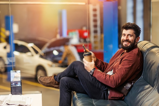 Männlicher Kunde wartet in der Werkstatt auf sein Auto und schaut in die Kamera