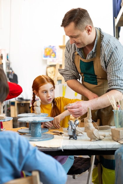 Männlicher Kunstlehrer, der Schürze trägt, die nahe seinem niedlichen Schüler steht