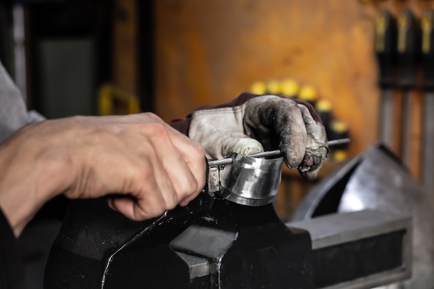 Männlicher Metallarbeiter, der ein Stück Metallbaugruppe konstruiert oder repariert. Mannhände, die mit Metallteilen in einer Werkstatt arbeiten